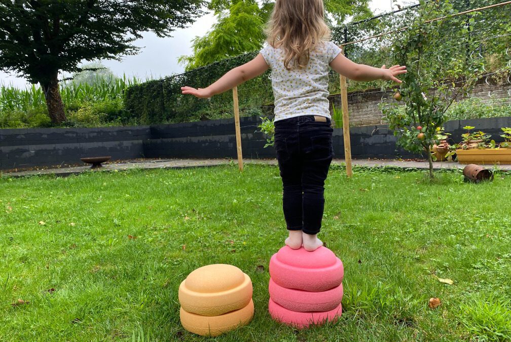 3 jarig kind staat op 3 gestapelde Stapelstein yoga te doen in de tuin.