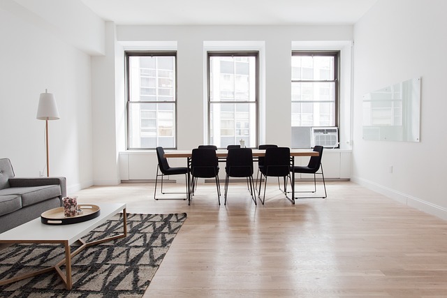 Strak ingerichte woonkamer met een tafel, eetstoelen en de juiste vloer. De woonkamer heeft 3 ramen en er ligt een mat op de grond.